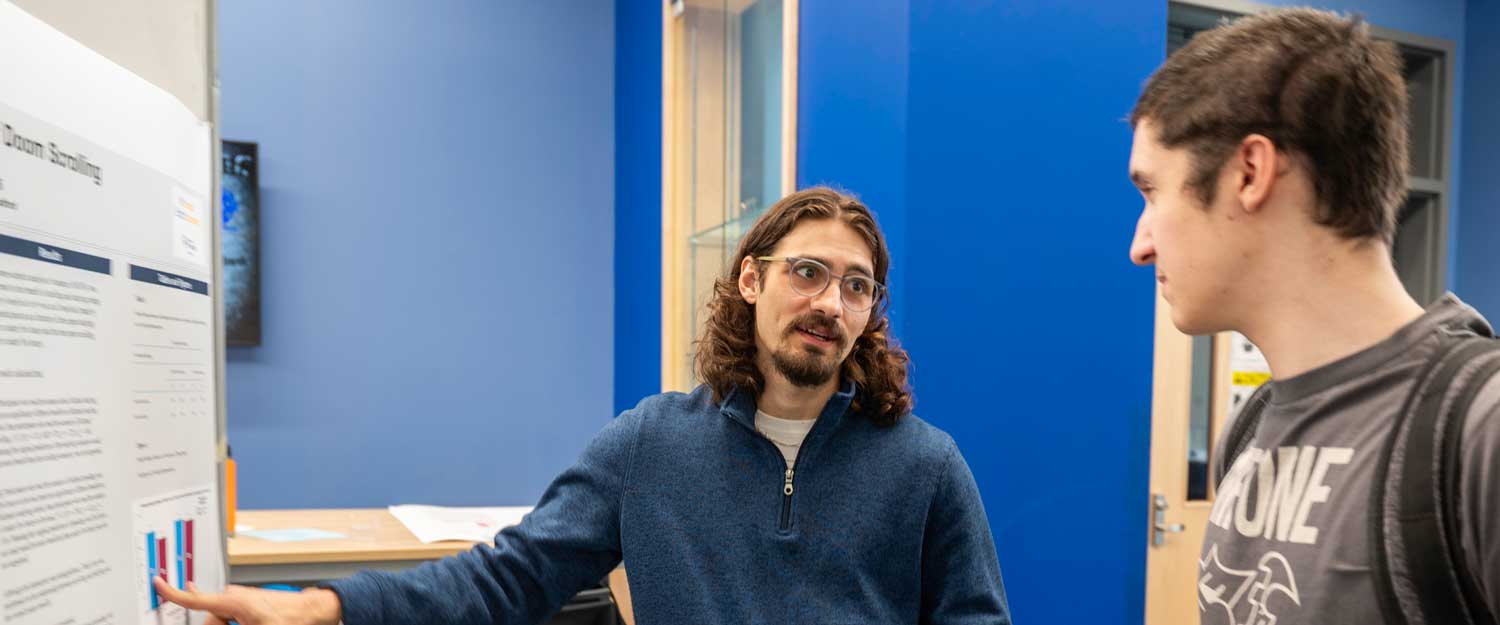 Student showing another student his research poster on Doom Scrolling